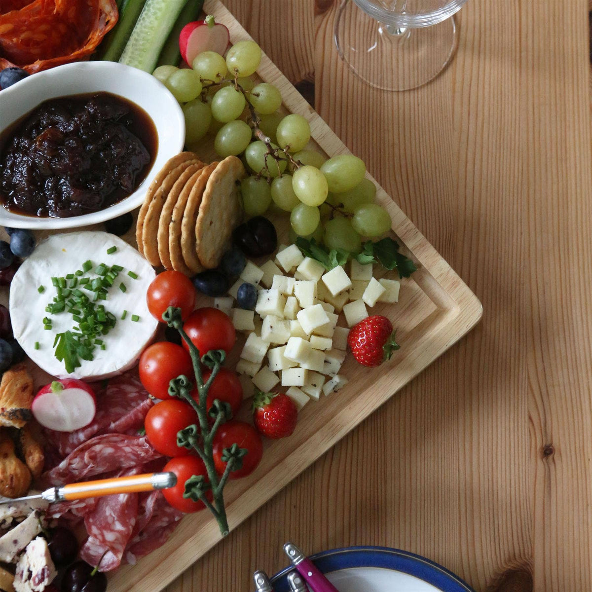 Detail of the 60 × 40cm rubberwood serving board with cubed cheese, green grapes, tomatoes, crackers and bowls of dip.
