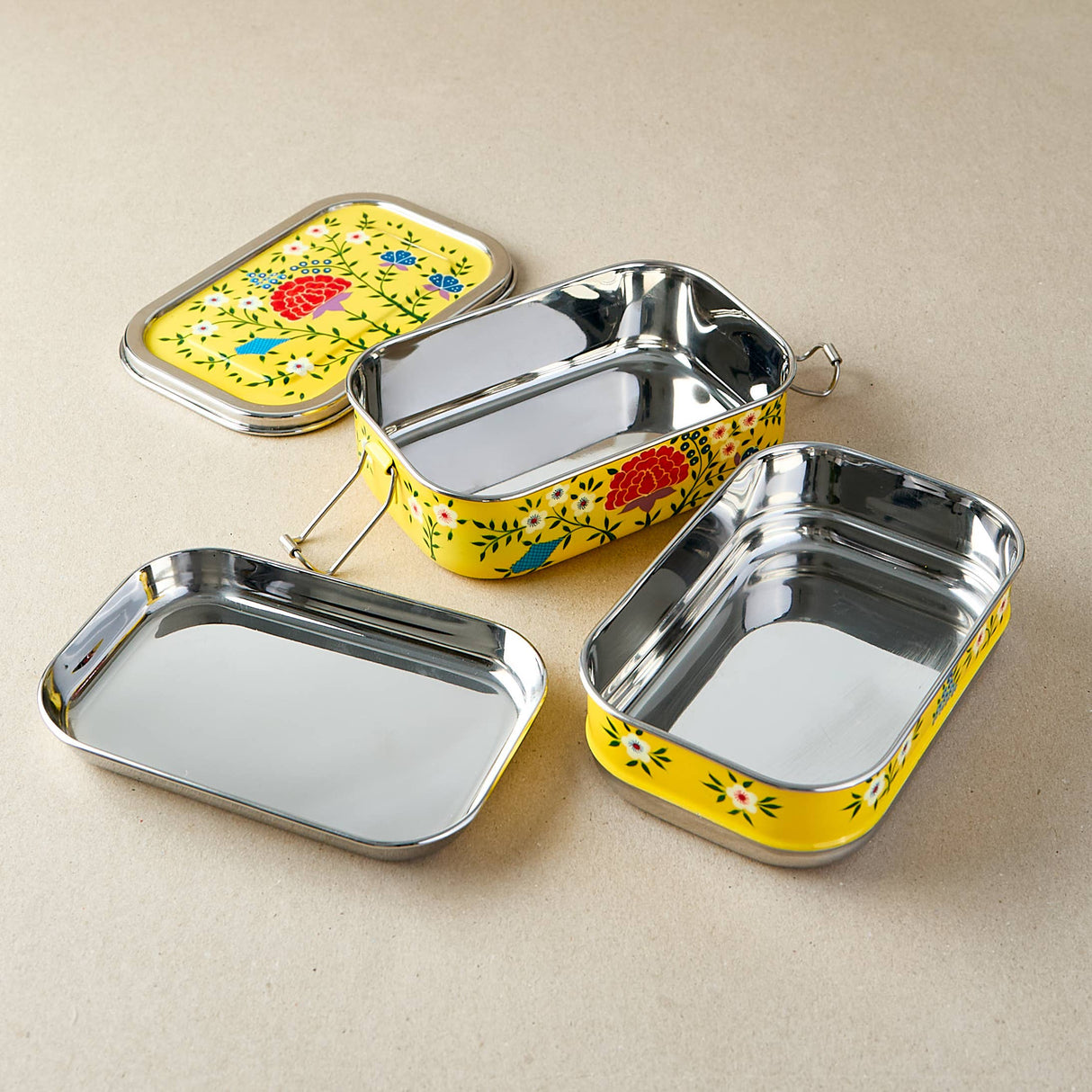 Set of three metal lunch boxes with floral designs on a beige background
