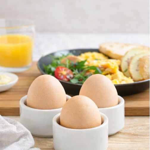 eggs in white cups with breakfast items like toast, orange juice,
