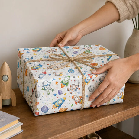 Space-themed personalised wrapping paper on a gift tied with twine, shown on a wooden shelf.
