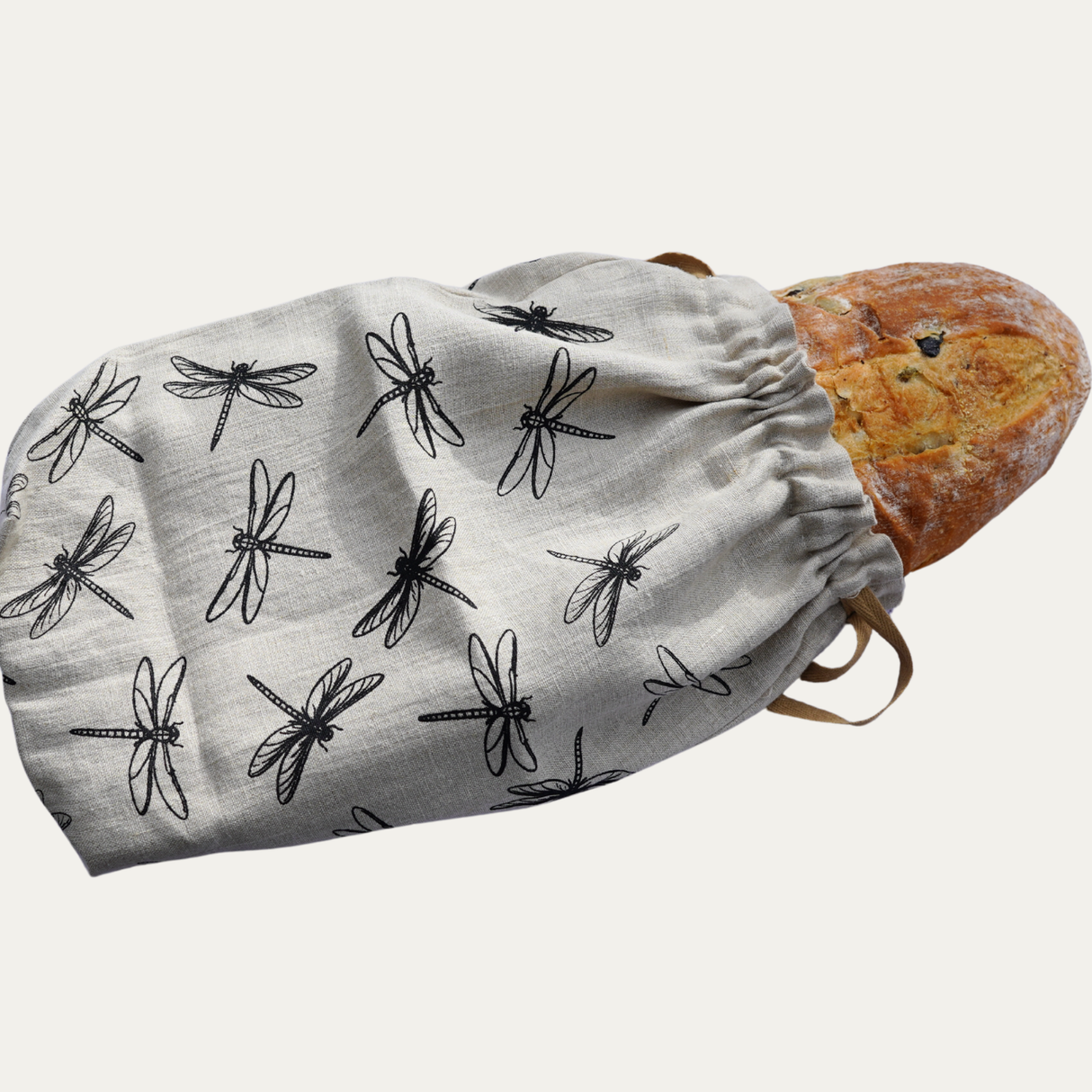 Reusable bread bag with dragonfly pattern containing a loaf of bread on a white background