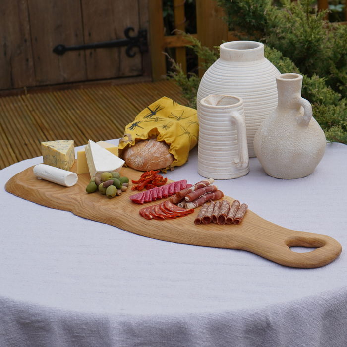 Wooden charcuterie board with meats, cheeses, and olives on a table with ceramic jars.