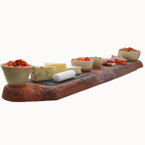 Wooden serving board with various food items including cheese and crackers on a white background