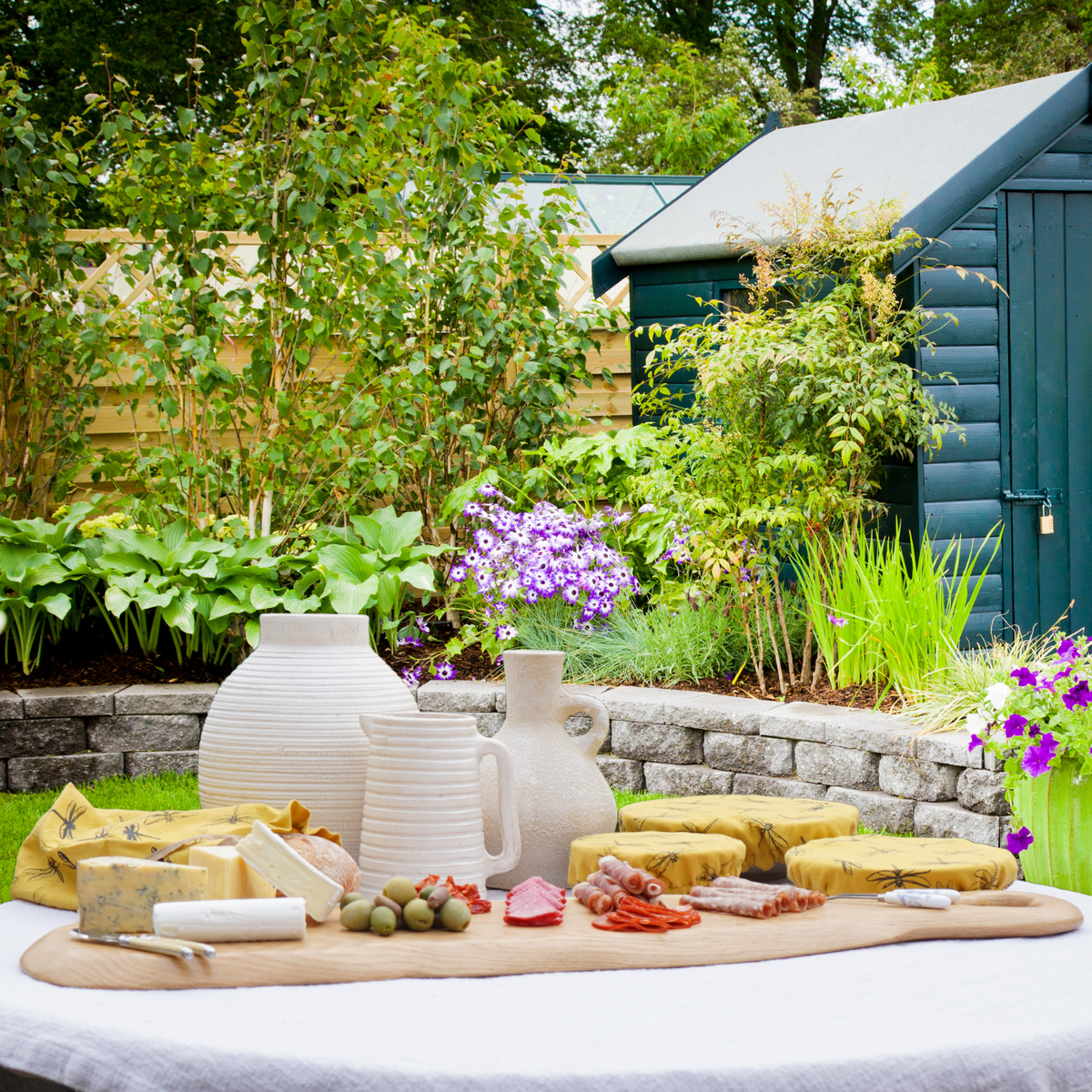 A long wooden sharing board set with food and small bowls on a garden table.