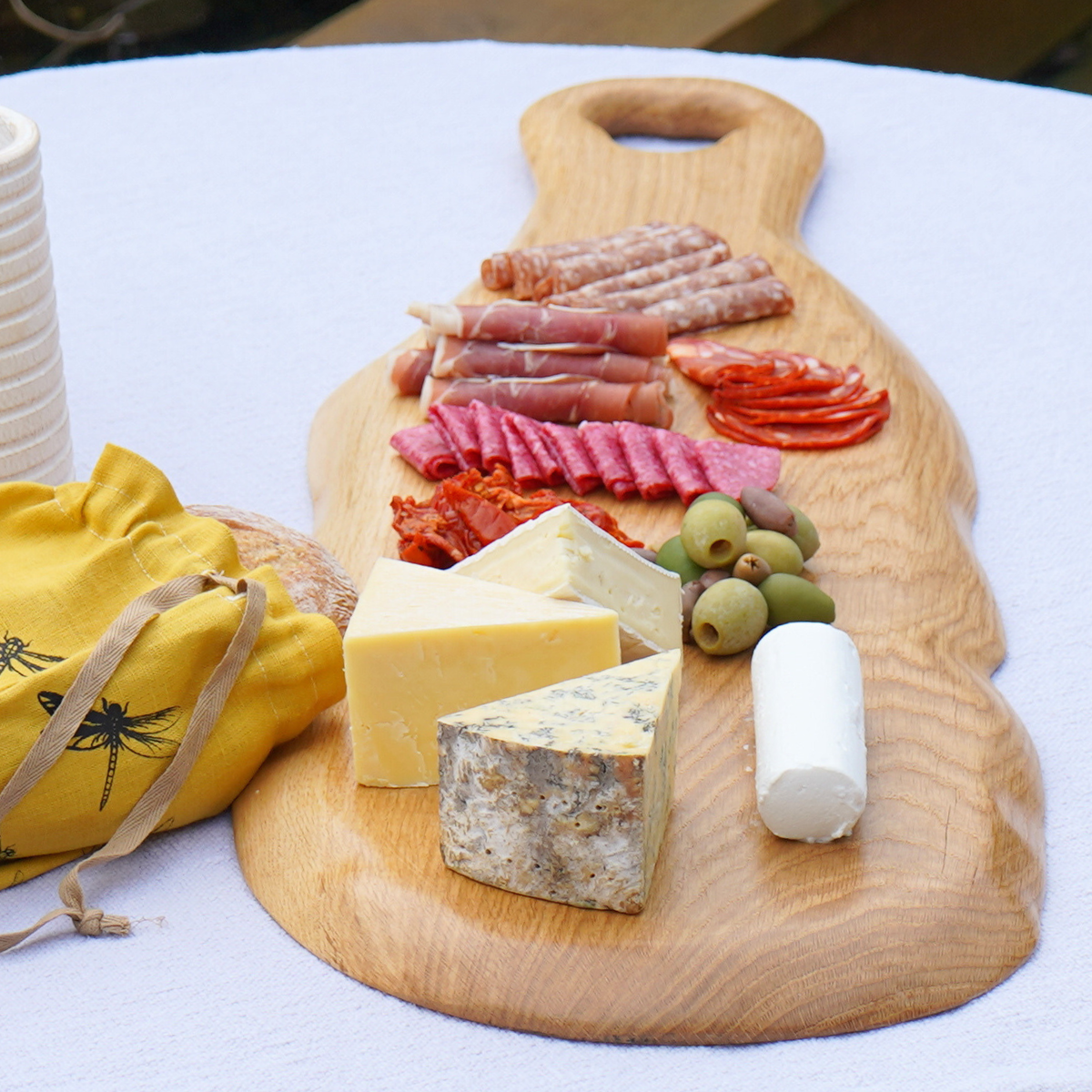 A long wooden serving board with cheese, cured meat and grapes.