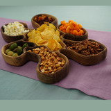 Assorted snacks in wooden bowls on a purple cloth with a green background