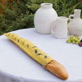 Baguette in a yellow bag with bee pattern on a white tablecloth with ceramic vases and grapes.