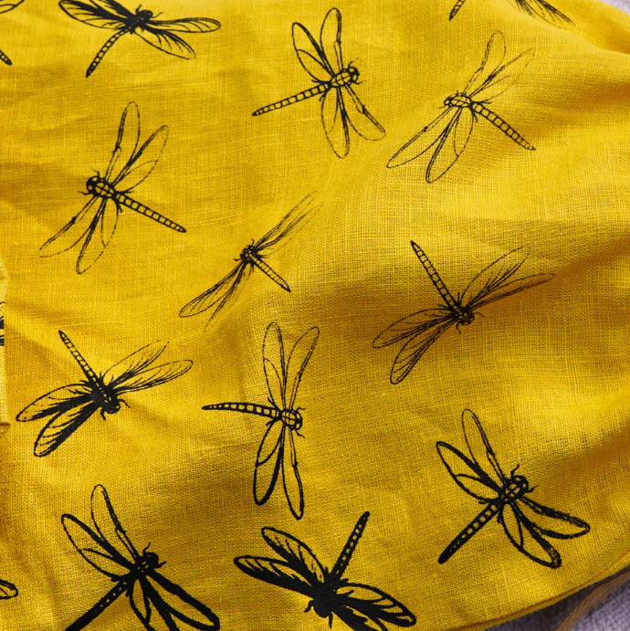Yellow drawstring bag with black dragonfly patterns next to a loaf of bread on a textured surface