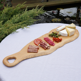 Wooden charcuterie board with meats, cheeses, and olives on a white surface outdoors.