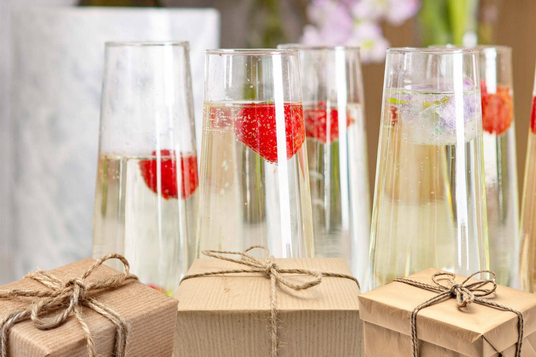 Clear glasses with red berries and champagne, tied with string, on a blurred floral background.