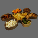 Wooden snack platter with various types of snacks including popcorn, chips, and nuts on a gray background.