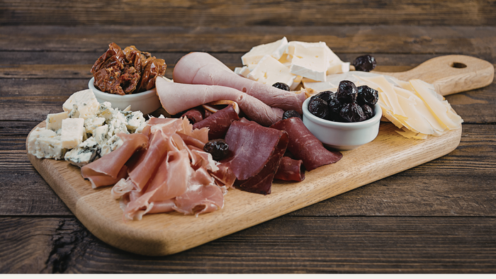 Wooden charcuterie board with meats, cheeses, and fruits on a wooden surface