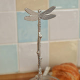 Decorative silver dragonfly on a branch with a tiled wall background