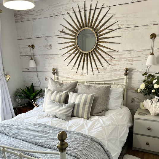 Cozy bedroom with white bed, sunburst mirror, and decorative pillows.