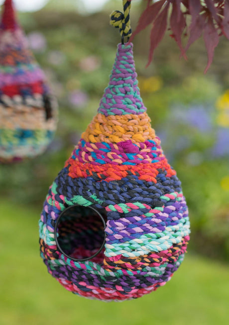 Colorful woven birdhouse hanging outdoors with blurred greenery in the background