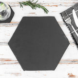 Hexagonal black placemat on a wooden table with cutlery and herbs.