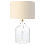Table lamp with clear glass base and beige fabric shade on a white background