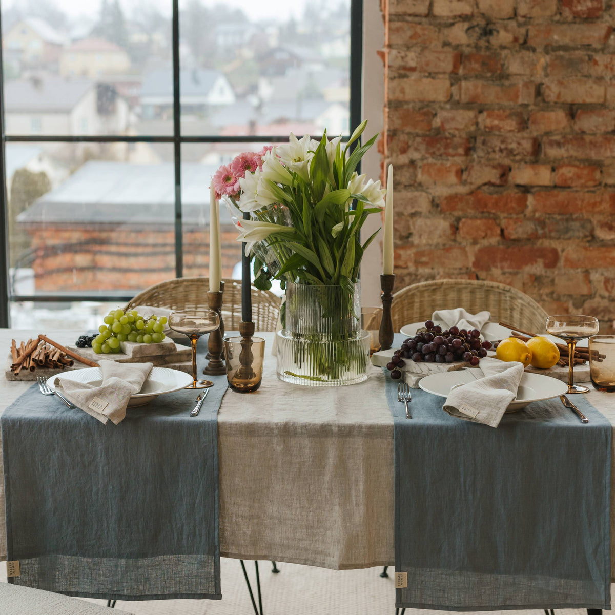 A linen table runner beneath flowers, serving dishes and glasses on a wooden dining table.