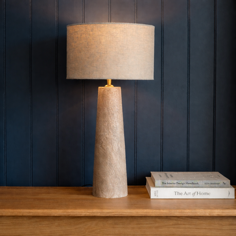 Textured table lamp on a wooden surface with books against a dark paneled wall