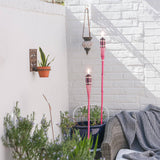 Outdoor setting with pink torches, plants, and a white brick wall.