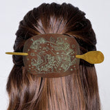 Decorative hair clip with animal designs on a person's hair against a white background