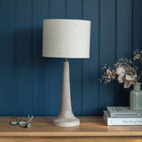 Table lamp with a textured white shade on a wooden surface against a blue paneled wall.