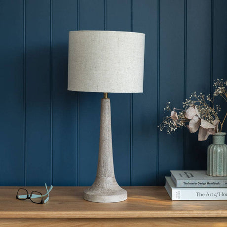 Table lamp with a textured white shade on a wooden surface against a blue paneled wall.