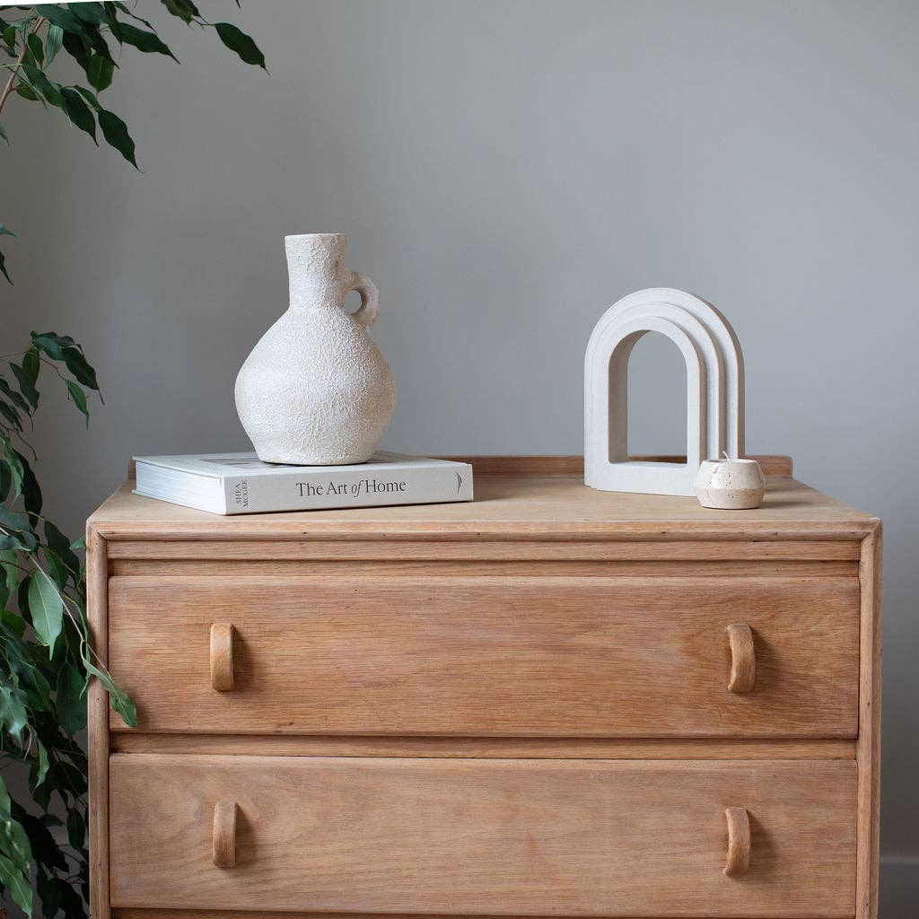 Wooden dresser with decorative items including a vase and book against a gray wall.
