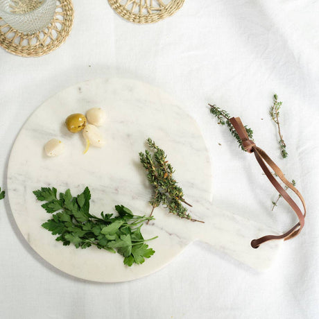 Marble cutting board with fresh herbs and a leather strap on a light background
