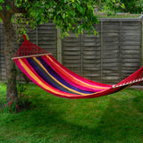 Colorful striped hammock hanging between two trees in a garden.
