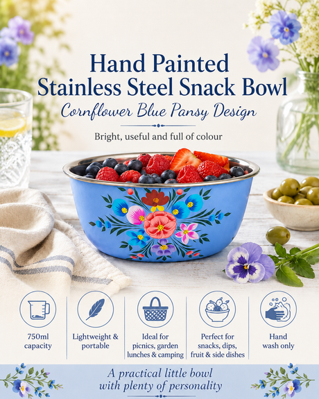Hand painted stainless steel snack bowl with cornflower blue pansy design on a table with flowers and fruit.