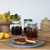 Jars of jam on a plate with bread, lemons, and a honey jar in the background.