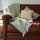 Green chevron patterned blanket draped over a brown leather sofa with beige pillows.