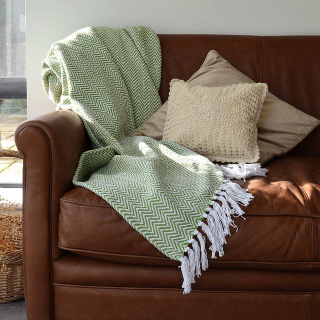 Green chevron patterned blanket draped over a brown leather sofa with beige pillows.