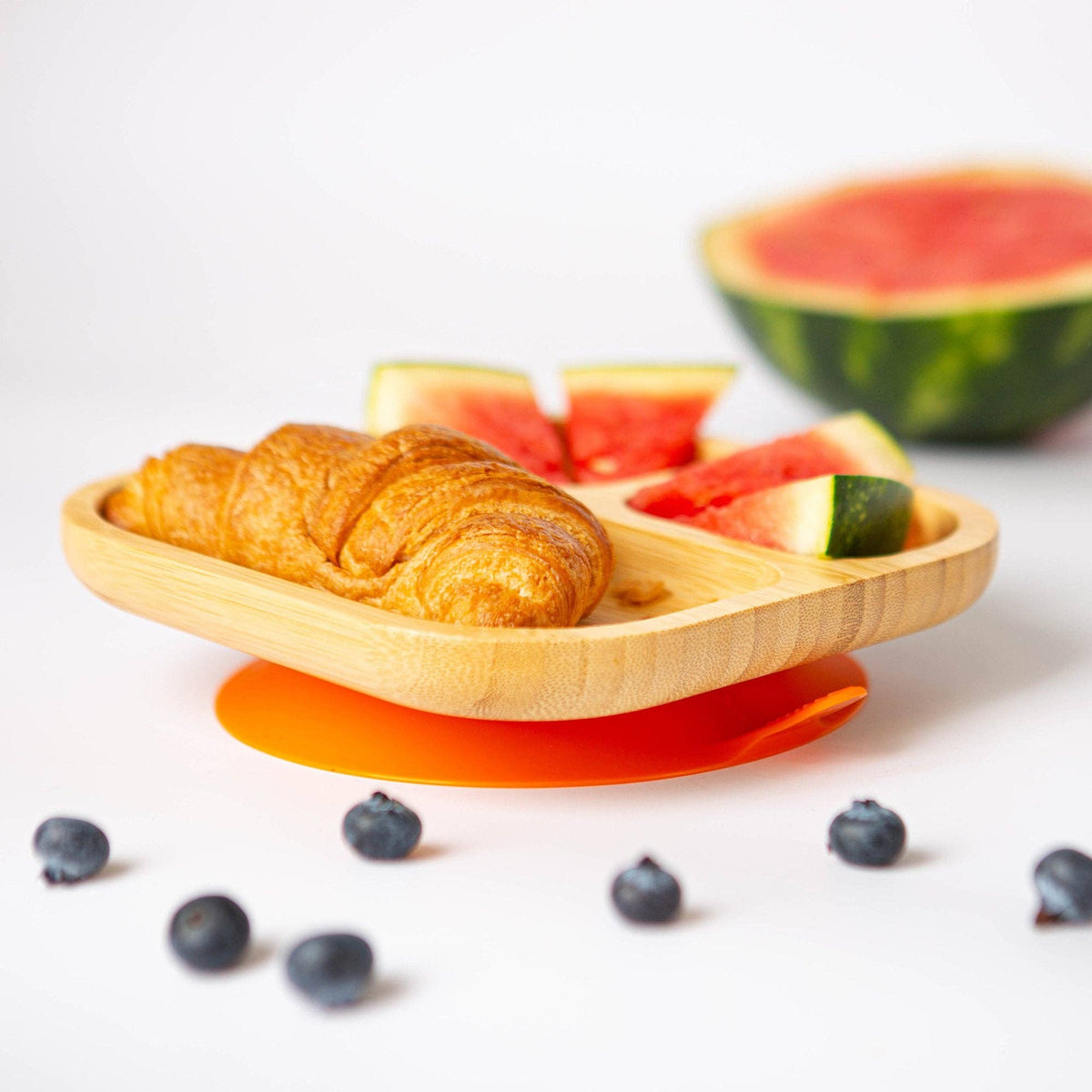 An orange-based divided bamboo plate with breakfast food, fruit and a small croissant.