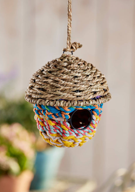 Colorful braided birdhouse hanging against a neutral background