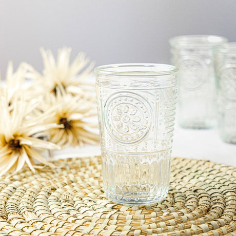 Decorative glass with floral pattern on a woven mat with flowers in the background