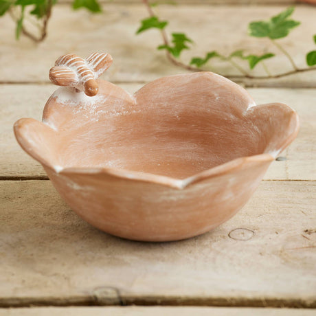 Terracotta bird bath on a wooden surface with plants in the background