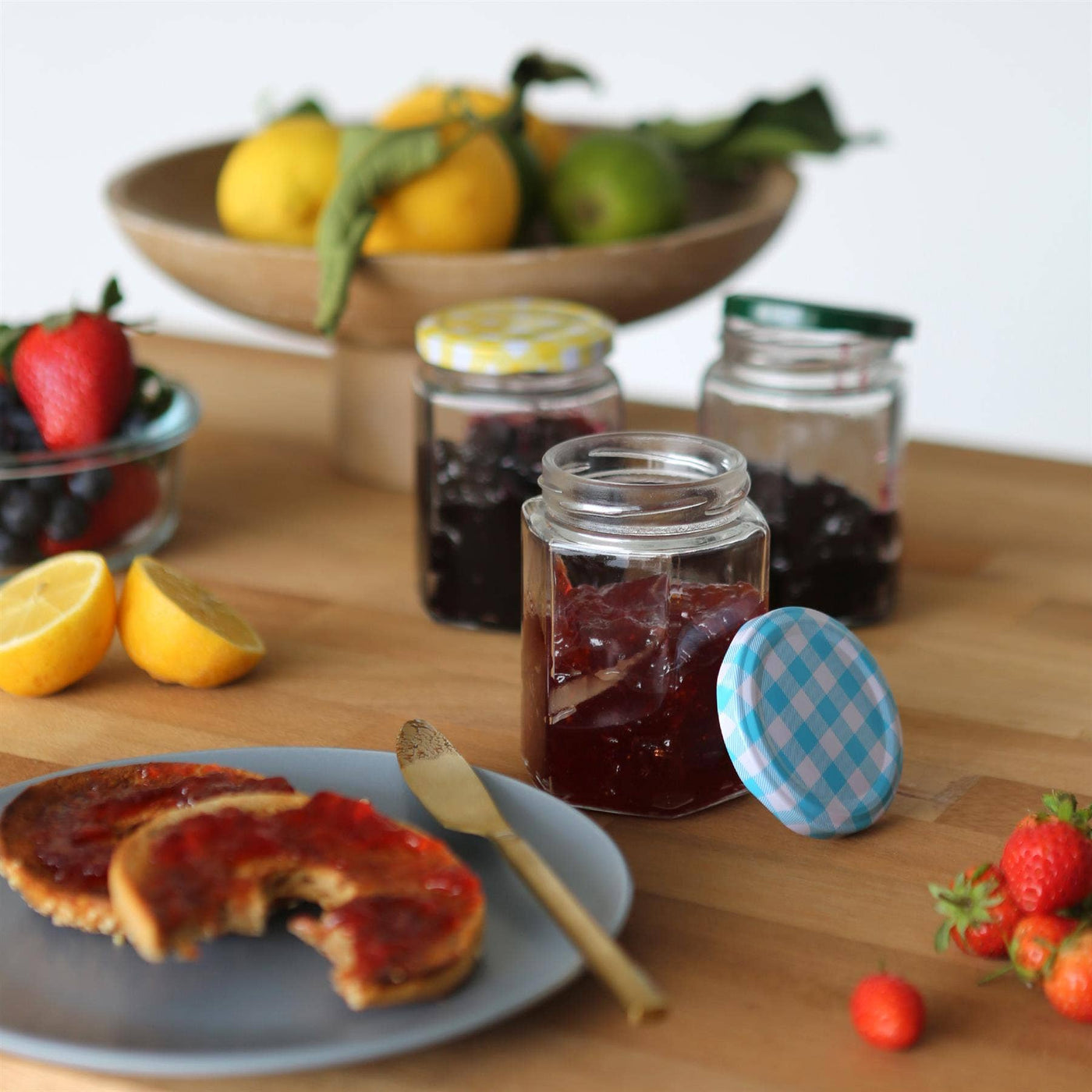 Jars of jam on a wooden table with fruit and pancakes.