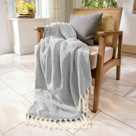 Grey chevron patterned throw blanket draped over a wooden chair with a cushion in a bright room.