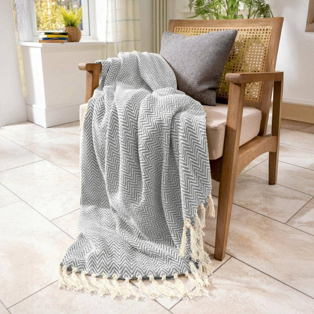 Grey chevron patterned throw blanket draped over a wooden chair with a cushion in a bright room.