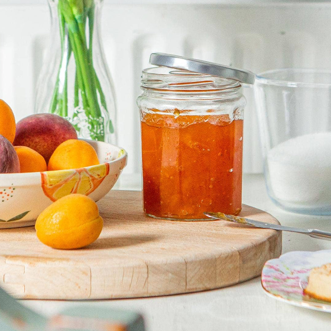 Table with a jar of jam, fruits, and pastries on a white surface.
