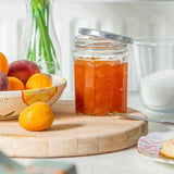 Table with a jar of jam, fruits, and pastries on a white surface.