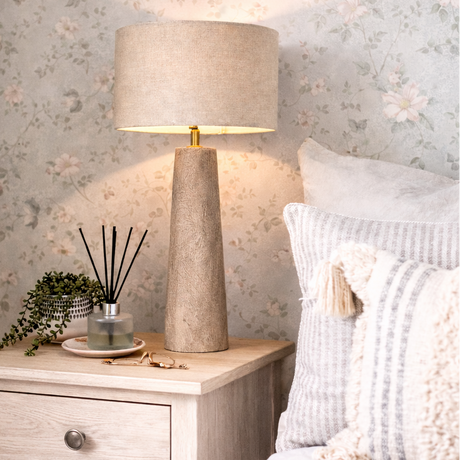 Nighstand with lamp, decorative items, and pillows against floral wallpaper.