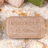 Bar of soap with 'Hoyar d'abricot' text on a sandy background with shells and plants.