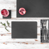Sleek black slate platter on a rustic wooden surface with a glass of pink drink and pomegranate.