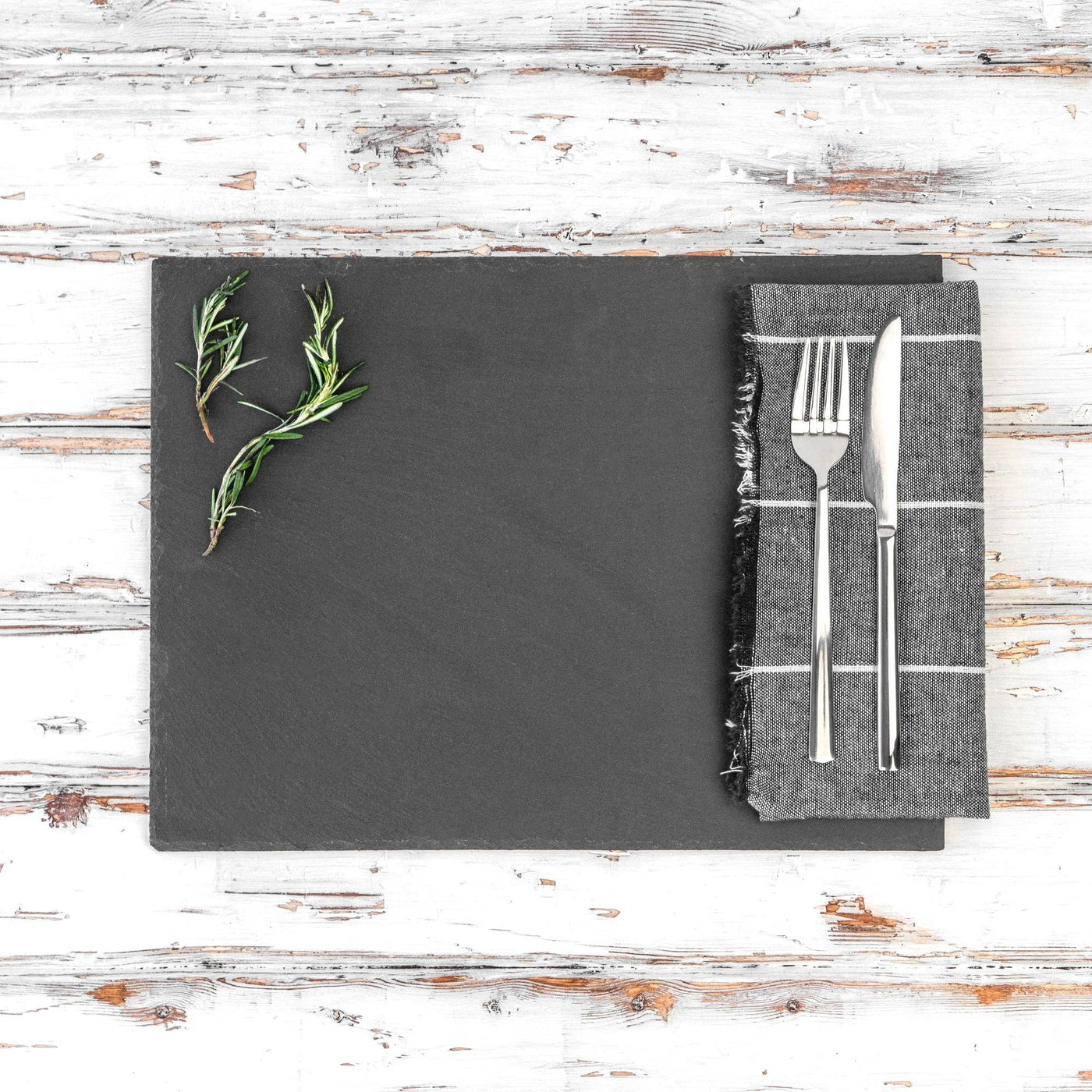 Slate platter with herbs and cutlery on a wooden surface
