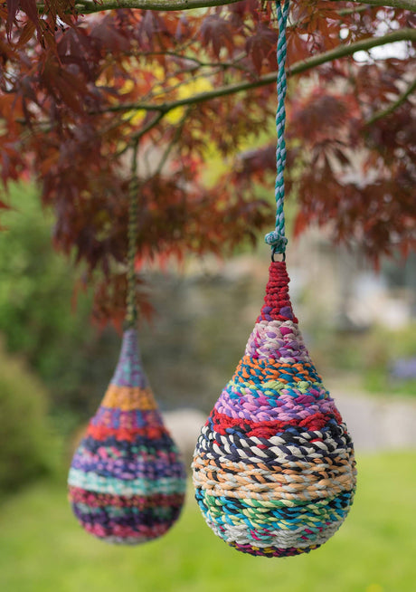 Colorful woven teardrop-shaped hanging decorations in a garden setting.