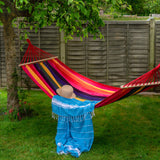 Person sitting in a colorful hammock under a tree with a wooden fence in the background