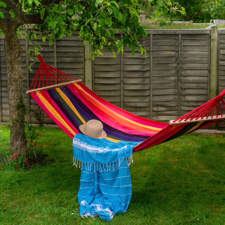 Person sitting in a colorful hammock under a tree with a wooden fence in the background